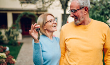 pareja-ancianos-con-llaves-en-mano-y-de-pie-delante-de-casa